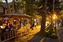Outdoor dining scene at sunset with people sitting at tables under large umbrellas